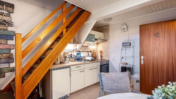 Una cocina compacta con escaleras de madera, una cama con almohada de diseño azul y blanco, y una puerta de madera con el número 12.