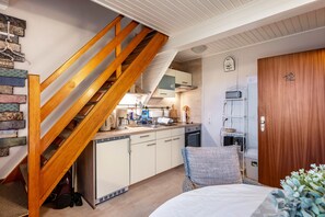 A compact kitchen with wooden stairs, a bed with a blue and white patterned pillow, and a wooden door with the number 12.