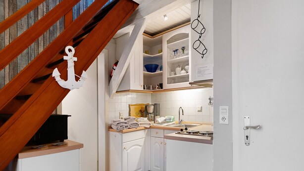 A kitchen with white cabinets, a wooden staircase, and a hanging kitchen towel rack. - Holiday Apartment 'Op'nböhn' with Shared Garden and Private Beach Chair (Nordstrand)