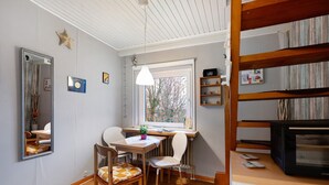 A room with a wooden table, two chairs, a mirror, a shelf with books, a television, and a window with a view of trees. - Holiday Apartment 'Op'nböhn' with Shared Garden and Private Beach Chair (Nordstrand)