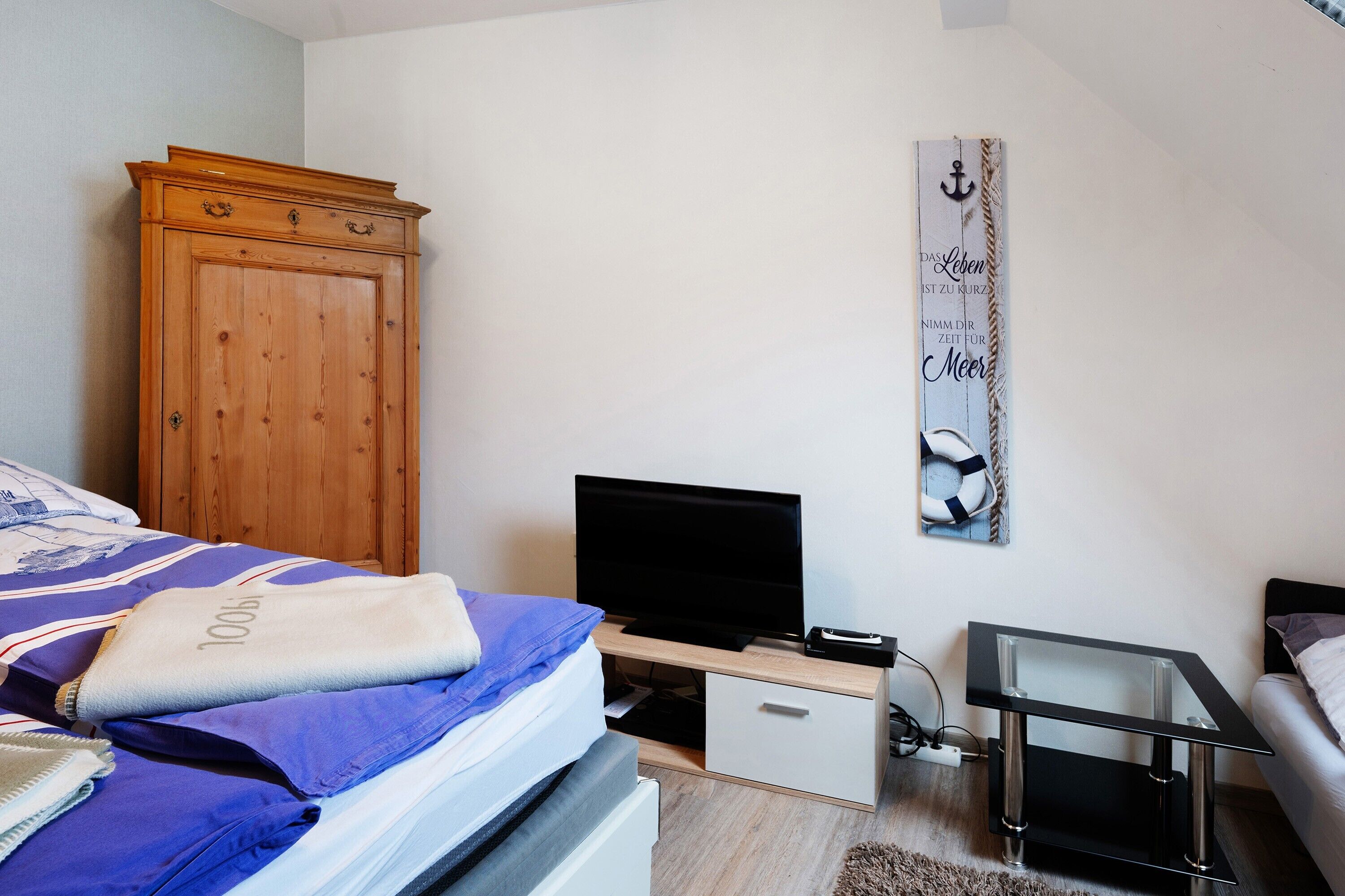 A bedroom with a bed, a television, a wooden wardrobe, a small table, and a wall decoration.