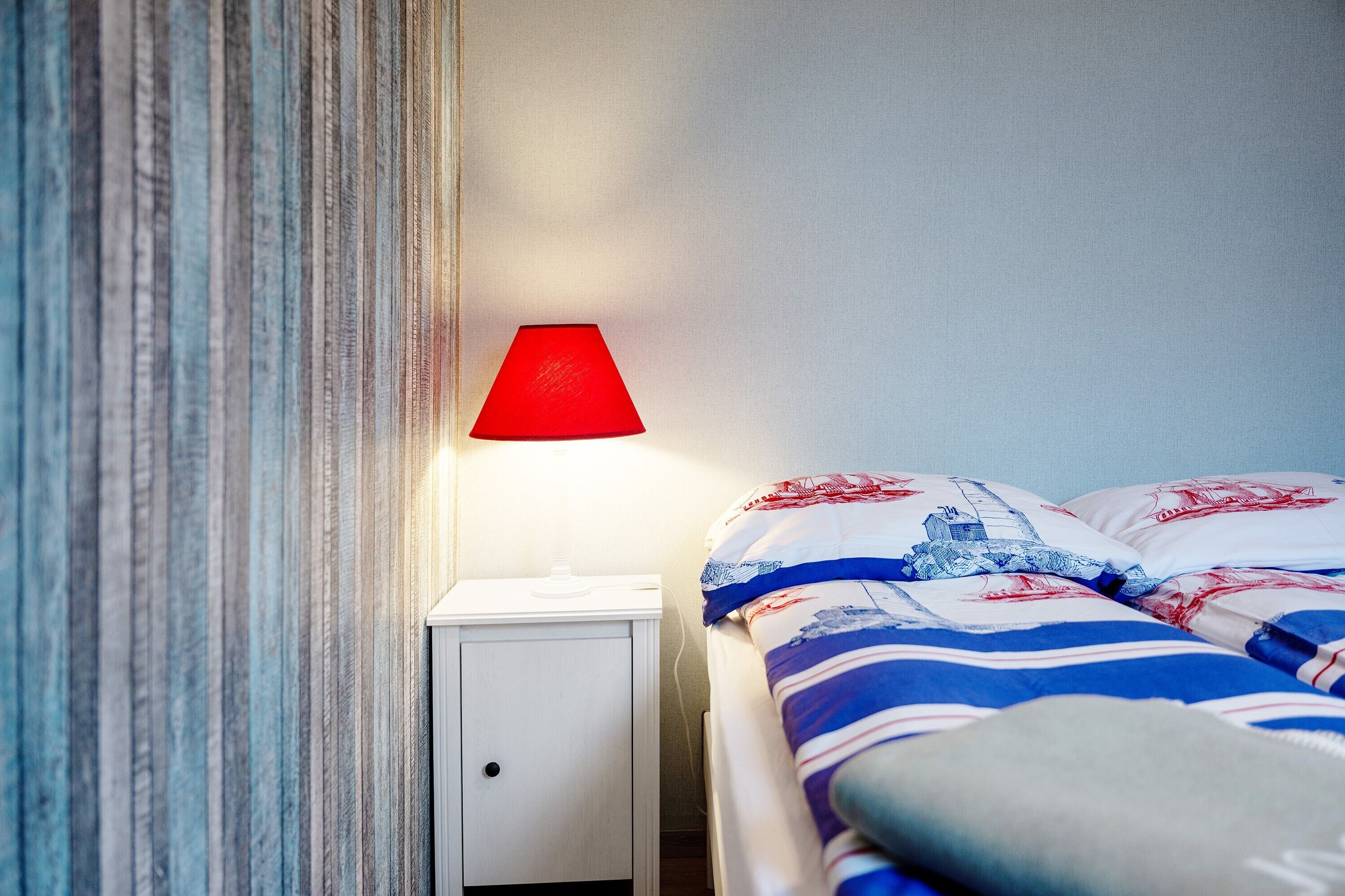 A bed with striped bedding, a red lamp on a bedside table, and a striped curtain.