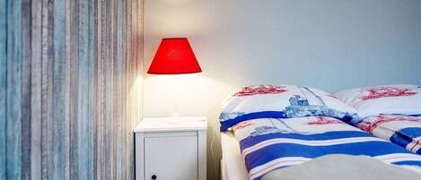 A bed with striped bedding, a red lamp on a bedside table, and a striped curtain.