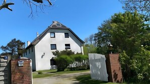 A white building with a sloped roof, a brick gate, and a gravel driveway. - Holiday Apartment 'Op'nböhn' with Shared Garden and Private Beach Chair (Nordstrand)