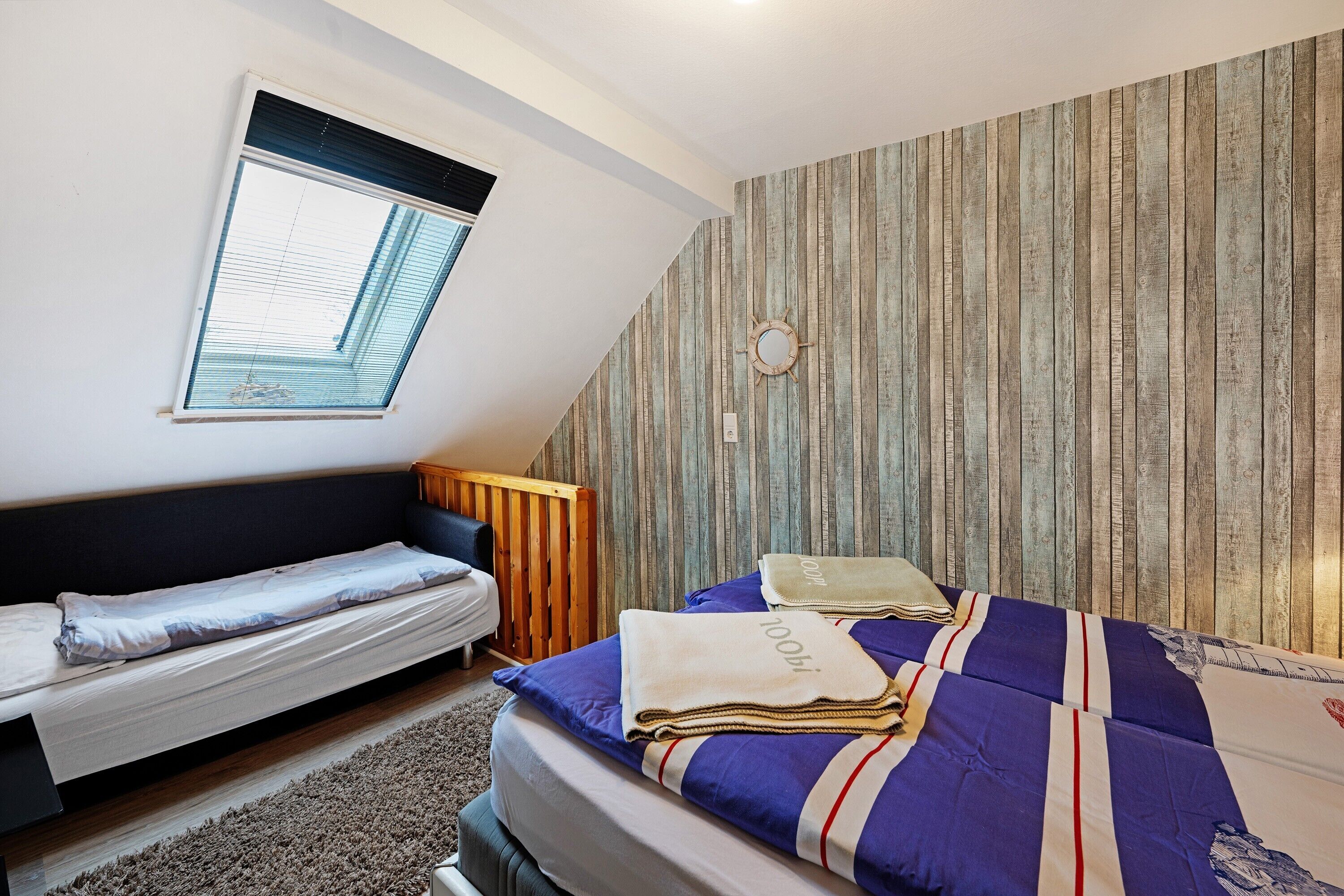 Une chambre à coucher comprenant un lit, un banc, une fenêtre et un mur recouvert de panneaux de bois verticaux.