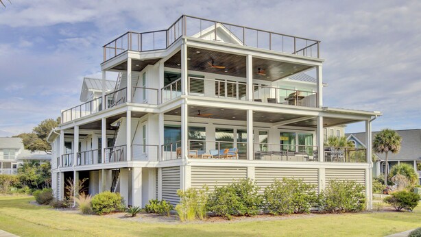 Una casa costera de varios pisos con balcones, ventanas amplias y un césped bien cuidado.
