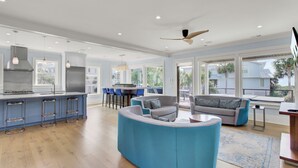 Un salón amplio con un sofá azul, una cocina con una isla grande y un balcón con vistas a palmeras.