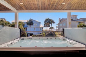 A hot tub with a wooden ceiling, surrounded by a pool, with a view of houses and palm trees.
