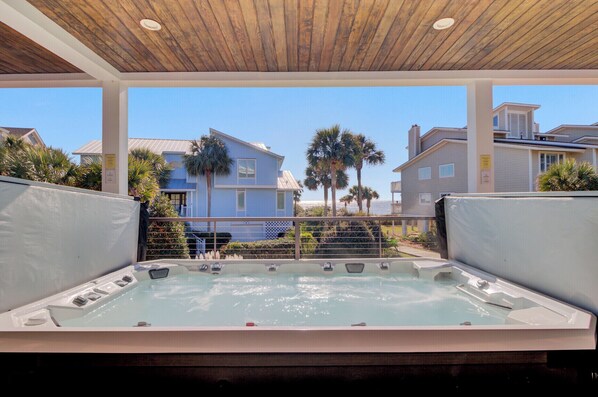 Zona de hidromasaje con techo de madera, rodeada por una piscina y con vistas a una zona residencial con palmeras y casas.