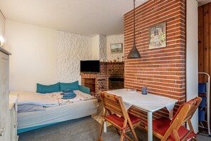 A room with a bed, a table with chairs, a brick wall, a fireplace, and a TV. - Studio 'Obendsünn' with Private Terrace and Shared Garden (Nordstrand)