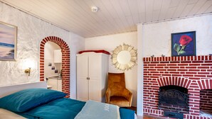 A bedroom with a bed, a red brick fireplace, a white wardrobe, and a mirror. - Studio 'Morgensünn' with Private Terrace and Shared Garden (Nordstrand)