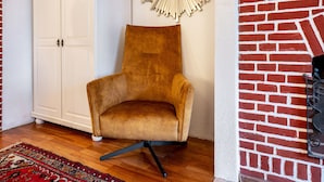 A room with a brown chair, a white wardrobe, a red brick wall, and a patterned rug. - Studio 'Morgensünn' with Private Terrace and Shared Garden (Nordstrand)