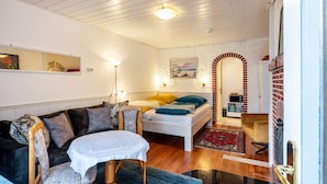 A cozy room with a bed, a sofa, a table, and a chair. - Studio 'Morgensünn' with Private Terrace and Shared Garden (Nordstrand)