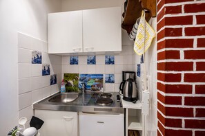 A compact kitchen with white cabinets, a stainless steel sink, a coffee maker, and a brick wall.