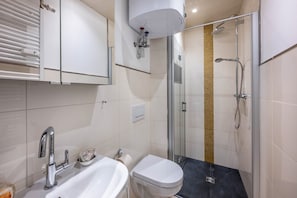 Moderni kylpyhuone, jossa on lasiseinällä varustettu suihku, valkoinen pesuallas ja wc.