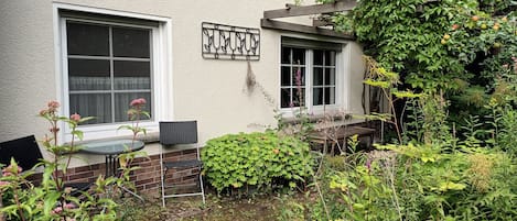 A garden with a table and chairs, a wooden bench, and a variety of plants and flowers.