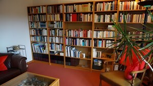 Een kamer met een boekenplank vol boeken, een leren bank, een glazen salontafel en een stoel.
