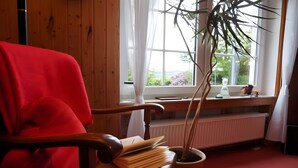 Een kamer met een houten stoel, een kamerplant, een radiator en een raam met uitzicht op groen.