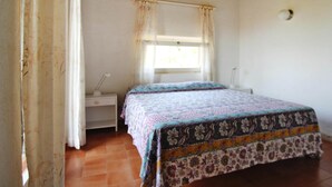 Un dormitorio con cama, cortinas, ventana, mesita de noche y lámpara.