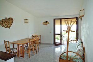 Un área de comedor con mesa y sillas de madera, un sofá con funda floral y un puerta corrediza de vidrio que da a un espacio exterior.