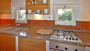 Una cocina con estufa a gas, lavamanos, armarios de madera y ventana con vista a árboles.