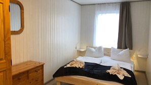 Un dormitorio con cama, cómoda de madera, lámparas de noche y ventana con cortinas.