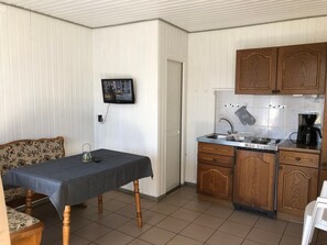 Una cocina compacta con armarios de madera, salpicadero de azulejos, un fregadero, una estufa y un televisor montado en la pared.