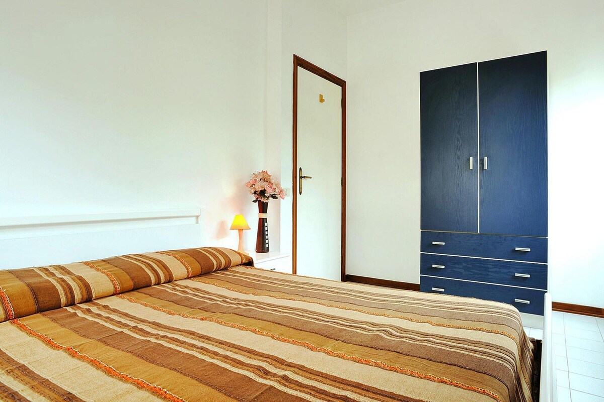 Une chambre à coucher avec un lit, une armoire, une table de chevet avec une lampe et un vase rempli de fleurs.