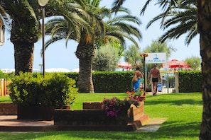 A well-maintained garden with palm trees and flower beds, a sign for 'LIDO MARLIN,' and a person walking in the distance.