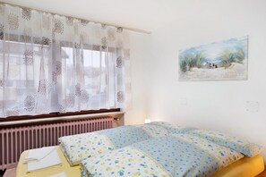 A bedroom with a bed, a window with sheer curtains, a radiator, and a wall-mounted painting.