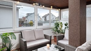 Una habitación acogedora con un sofá, una mesa con una vela y amplias ventanas con vistas a una zona residencial.