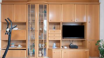 Ein Wohnzimmer mit Fernseher, Holzschränken, Laufband und Topfpflanze.