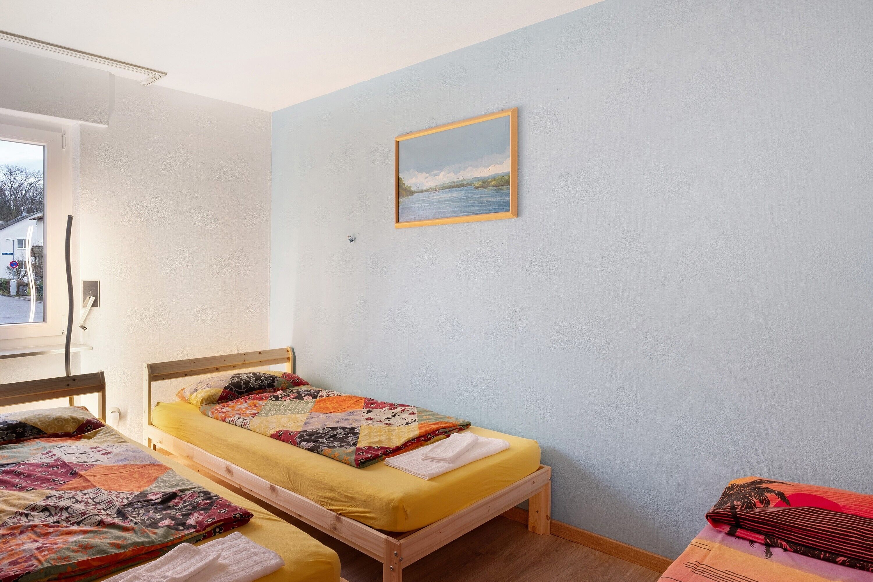 A room with two wooden beds, one with a quilt and the other with a yellow sheet.