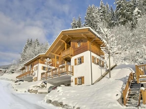 A multi-story wooden chalet with balconies, surrounded by snow-covered trees.