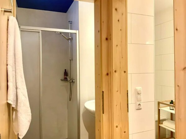 Une salle de bain avec douche, toilettes et un mur recouvert de panneaux en bois.
