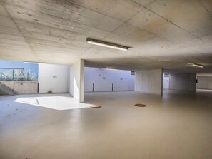 An empty parking garage with concrete pillars, a flat floor, and a view of a bridge outside.