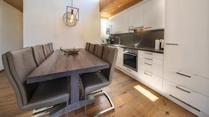 Una cocina moderna con armarios blancos, horno empotrado y comedor con mesa y sillas de madera.