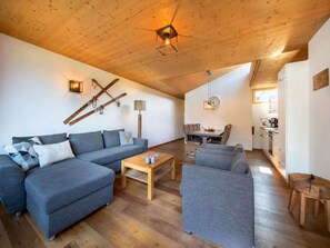 A modern living room with a wooden ceiling, a sofa set, a coffee table, and a dining area with chairs.