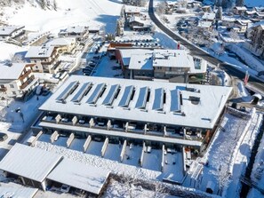 A multi-story building with a flat roof, surrounded by snow-covered ground and other buildings.
