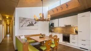 A modern kitchen with wooden cabinetry, a dining area with benches, and a chandelier. - Contemporary Alpine Stay in Neukirchen (Neukirchen am Großvenediger)
