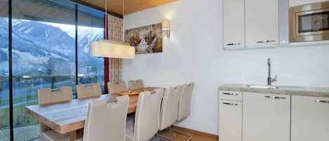 Una cocina moderna con armarios blancos, microondas integrado y una zona de comedor con mesa y sillas de madera.