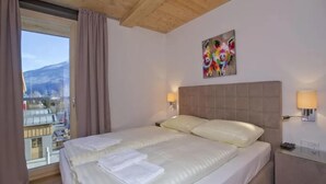 A hotel room with a large bed, two bedside lamps, a painting on the wall, and a view of the city through the window.