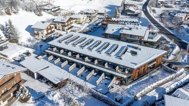 A snow-covered hotel with multiple buildings, a parking lot, and a mountainous backdrop.