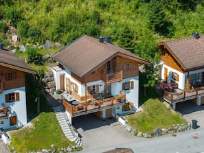 A residential area with three houses featuring wooden exteriors, balconies, and a stone pathway.
