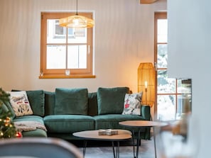 A cozy living room with a green sofa, a small round table, and a large window with a view.