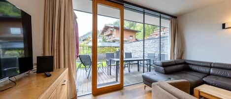 A modern living room with a wooden desk, a television, a sofa, and a sliding glass door leading to an outdoor patio.