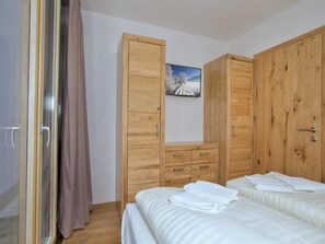 Een slaapkamer met twee bedden, houten kasten, een schilderij en een gordijn.