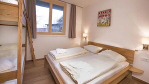 Une chambre avec des lits superposés, une fenêtre avec des rideaux, un tableau au mur et une lampe de chevet.