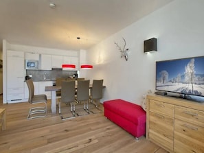 Een moderne keuken met witte kasten, een magnetron, en een eethoek met stoelen en een rode poef.