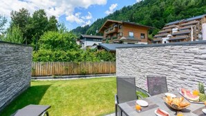 Une terrasse avec une table préparée pour le petit-déjeuner, un mur en pierre et une vue sur une montagne et des bâtiments.